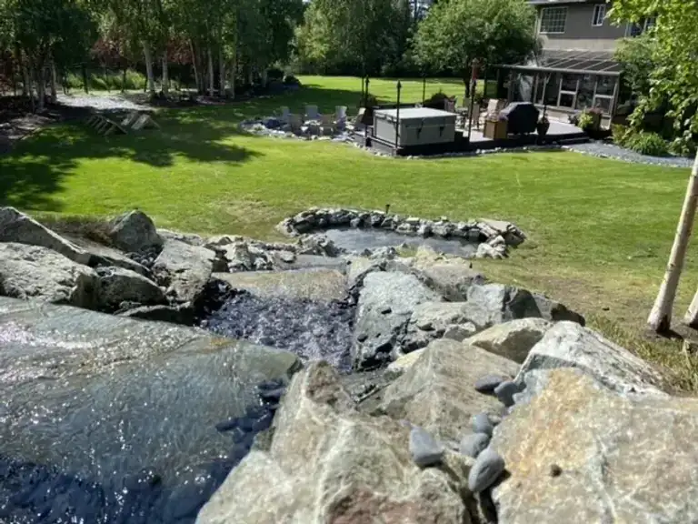 Boulder-lined stream running through a lawn towards a covered seating area