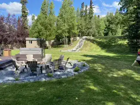 Backyard fire pit and lounge chairs beside a boulder stream and open lawn